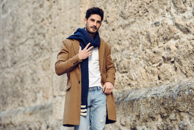Man in winter coat and scarf standing next to Spanish wall