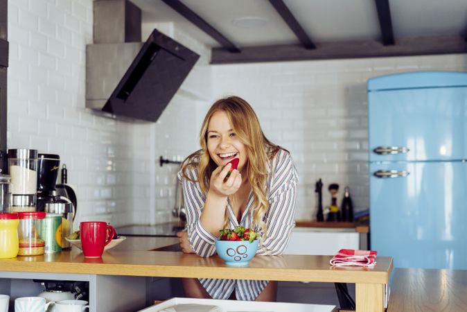 Young female eating strawberry in kitchen