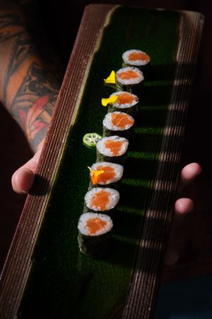 Crop waiter showing sushi rolls on wooden tray