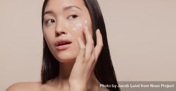 Close up of a youthful female model applying moisturizer to her face 5qq2j5