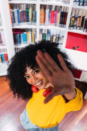 Cheerful woman gesturing stop sign and smiling in library