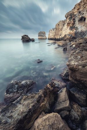 Still water near rocks under cloudy sky