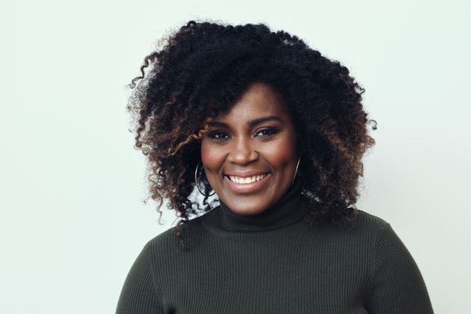 Portrait of a Black woman smiling in studio shoot in a green turtleneck