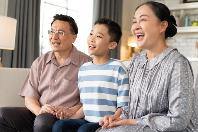 Happy Asian grandson and grandparents relax sitting on couch in the living room