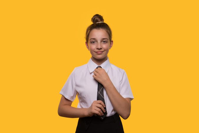 Teen girl adjusting tie in school uniform, smiling, standing confidently
