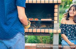 Man cooking sausages and vegetable skewers in a barbecue 0WOOLy