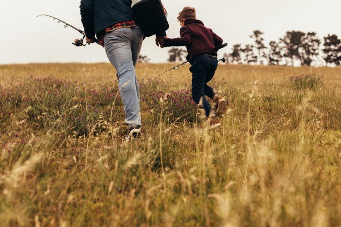 Low shot of father and son walking uphill with fishing gear