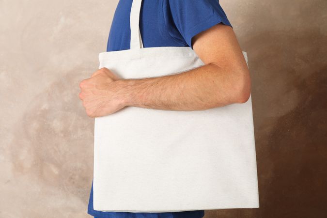 Young man holding tote bag against brown background, empty space