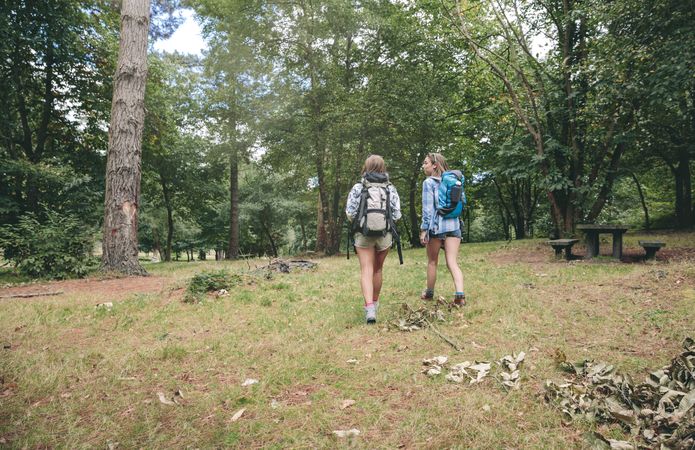 Two women friends with backpacks walking in forest