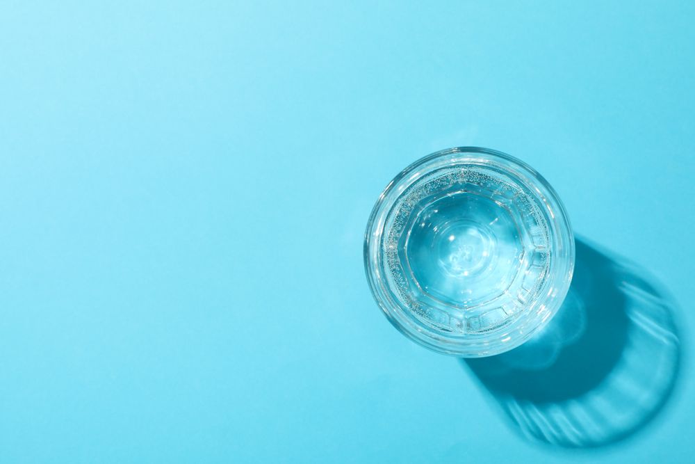 Looking down at full glass of water in blue room, copy space