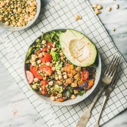 Healthy vegan lunch bowl with avocado, grains, vegetables, on checkered napkin, square crop