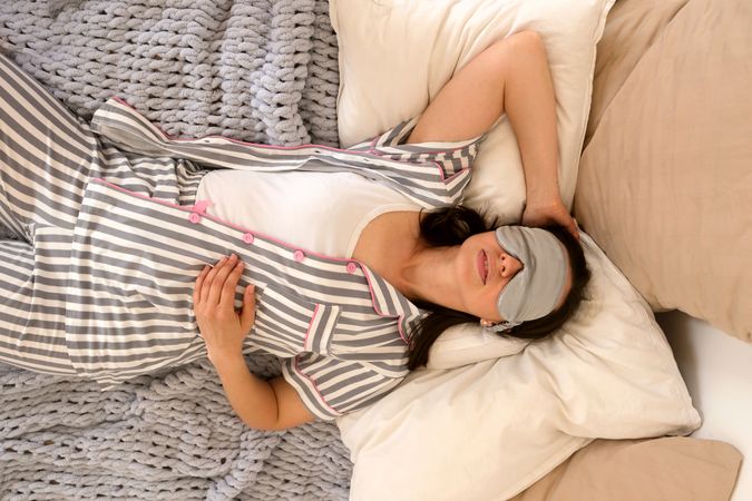 Woman sleeping in bed, hand on cheek, with eye mask.