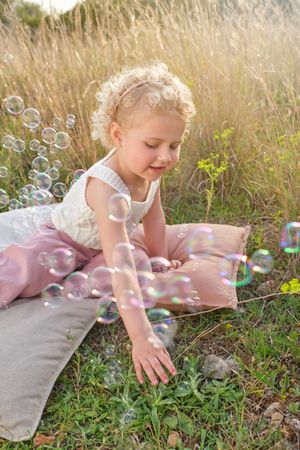 Happy girl playing with soap bubbles in sunny countryside