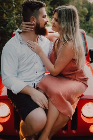 Loving couple sitting on car on road near forest