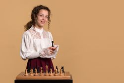 Young girl smiling while holding chess piece in hand.