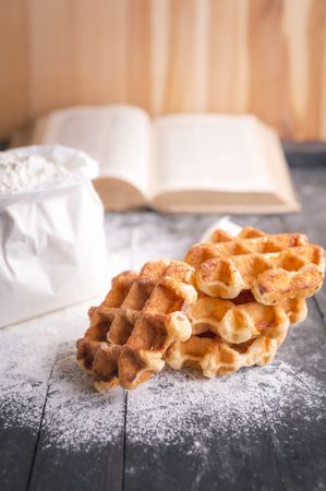Homemade Belgian waffles with flour bag and open cookbook on rustic table