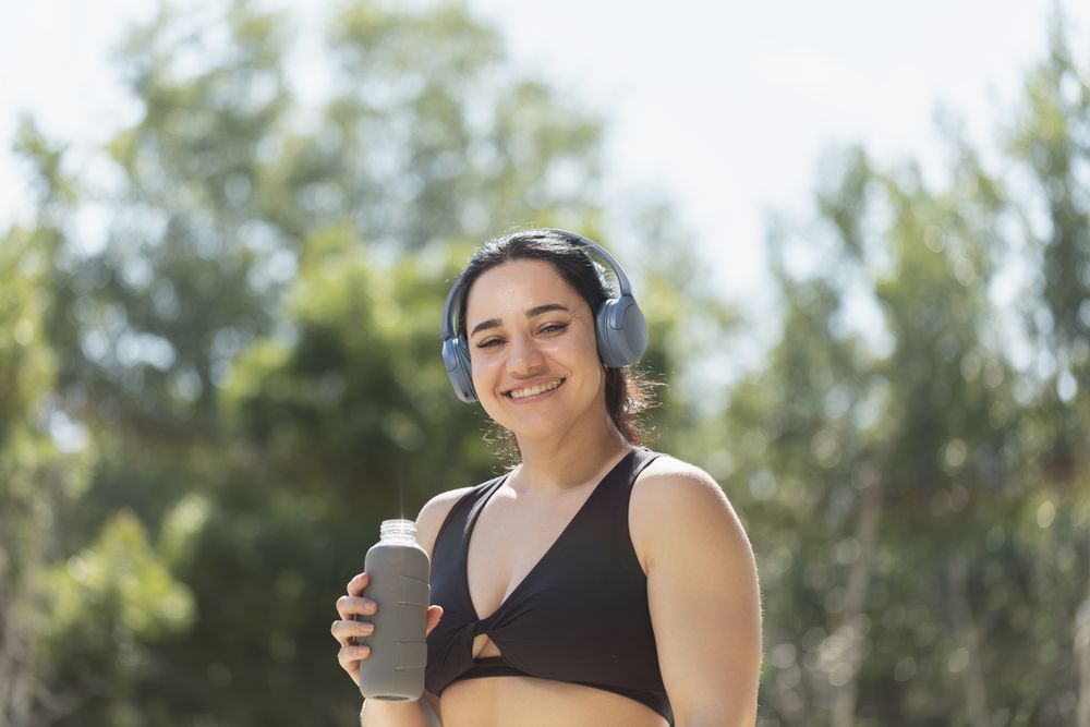 A young girl smiles while drinks water to hydrate herself, from a reusable bottle, during a morning exercise session