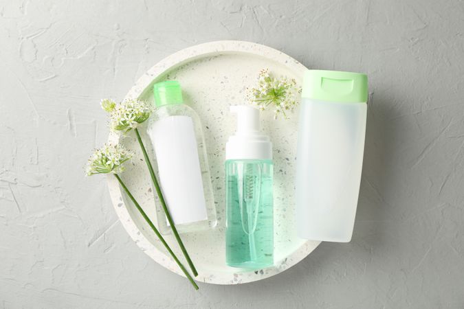 Liquids for body care in different bottles and allium flowers on blank background