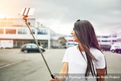 Woman looking away from selfie stick as she takes photo of herself bxLABb