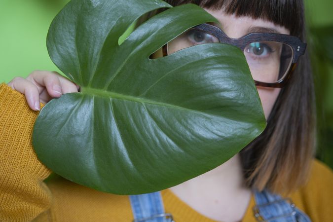 Portrait of woman in orange sweater covering her face with tree leaf