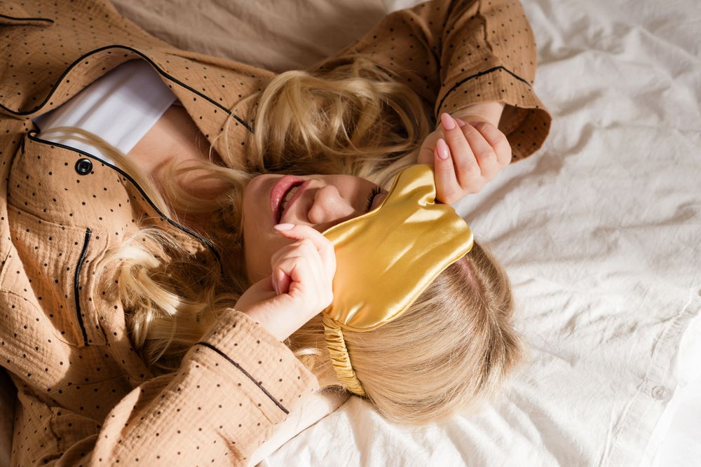 Smiling woman lying on bed, covering eyes with headband.