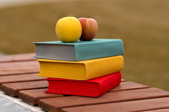 Two apples placed on stack of colorful hardcover books.