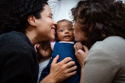 Close up of two moms kissing a baby girl while lying on the bed