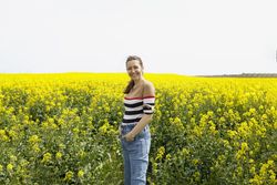 Smiling woman in jeans in yellow field on overcast day