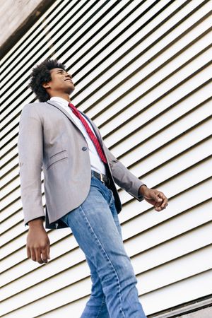 Man in jeans and dress shirt with tie walking outside next to wall