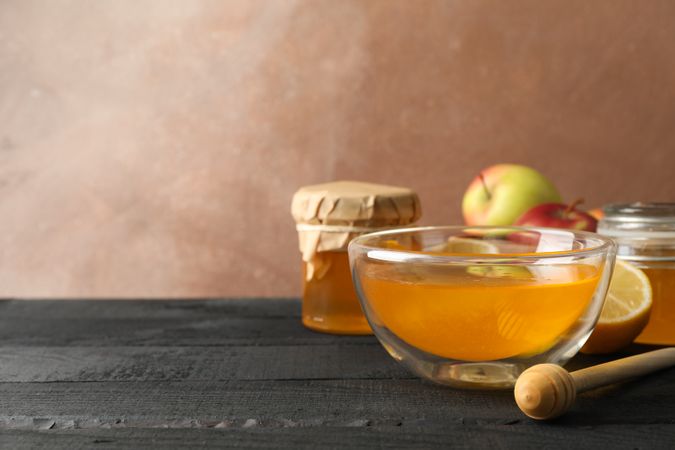 Bowl with honey, dipper and fruits on wooden background, space for text