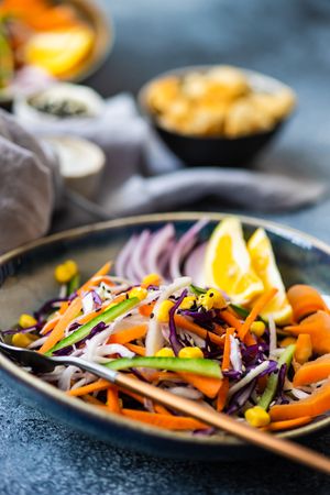 Close up of healthy vegetable salad and lemon slices in bowl on counter with copy space