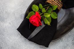 Top view of table setting with red rose on dark plate