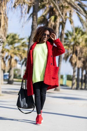 Smiling female in sunglasses with curly hair walking on palm tree lined street