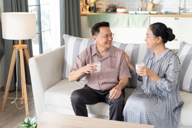 Happy Asian mature couple holding glass of milk and drinking together