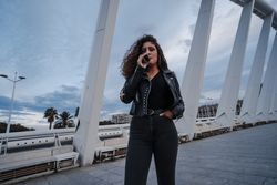 Stylish woman in jacket and jeans smoking on bridge