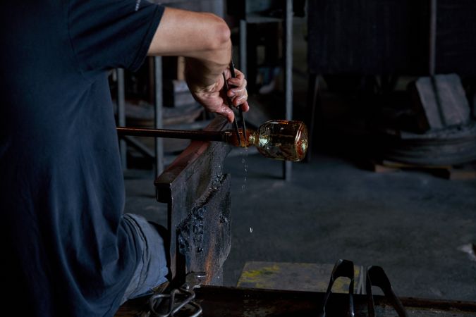 Crop man making glass using rod and tongs in workshop