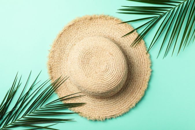 Straw hat and palm branches on mint background, top view