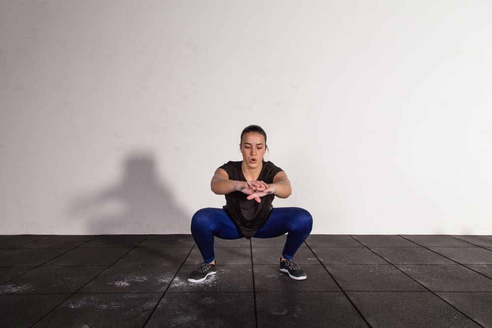 athletic young woman in sportswear doing squats in gym