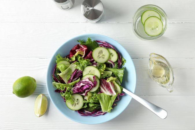 Plate with fresh salad, spices and oil on wooden background, top view