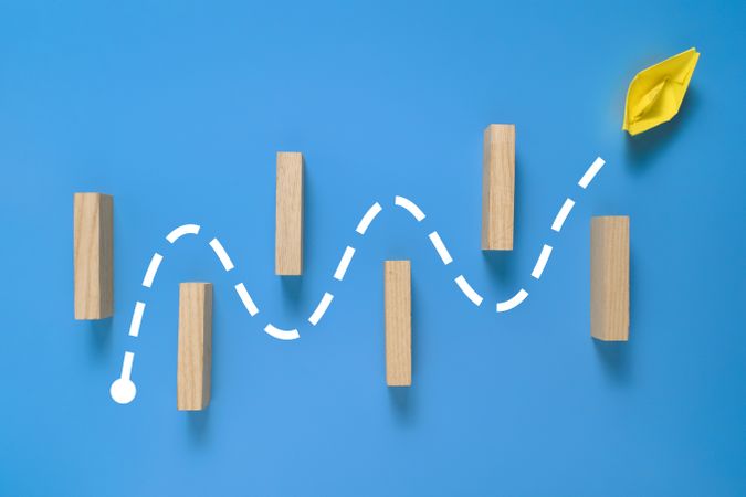 a yellow paper boat passes through barrier. isolated on blue background.