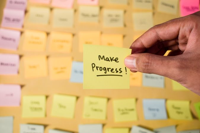 Hand hold sticky notes with words Make Progress
