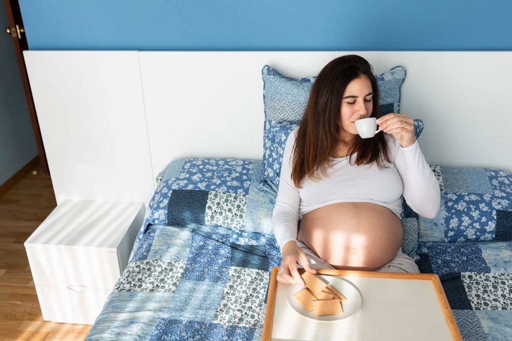 Tender pregnant woman having breakfast on bed