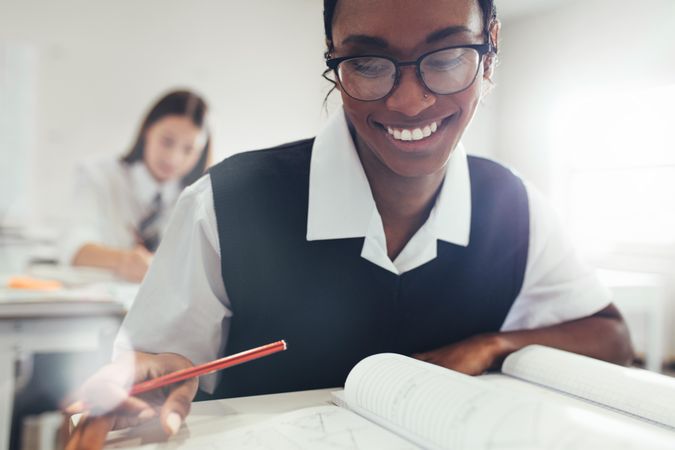 Teenage girl wearing eyeglasses sitting at desk in classroom in high school