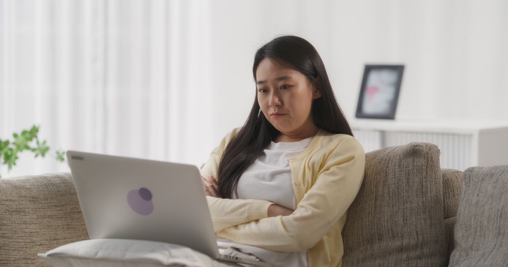 Young Asian Female Browsing Internet, Using Laptop Computer at Home