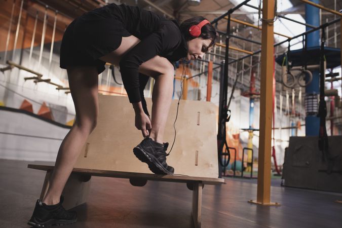 Smiling woman with headphones lacing shoe in gym