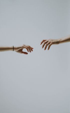Two hands about to touch against light background