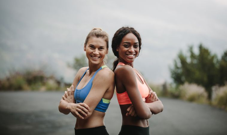 Fit women standing with back against each other with crossed arms