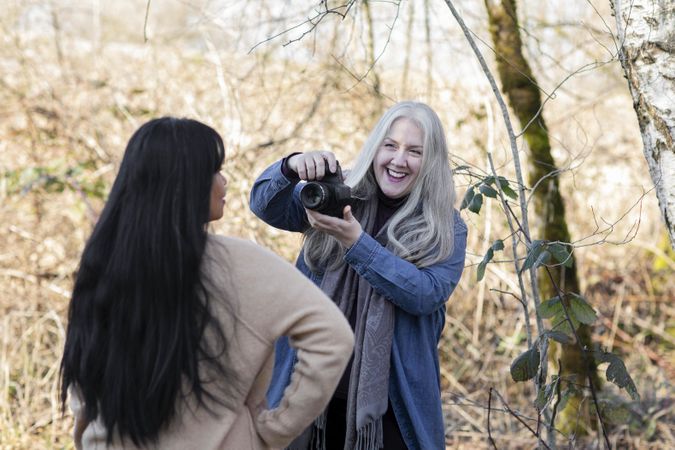 Older woman smiling and photographing another woman in the woods