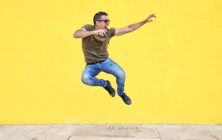 Smiling male jumping in front of yellow wall and looking to the side