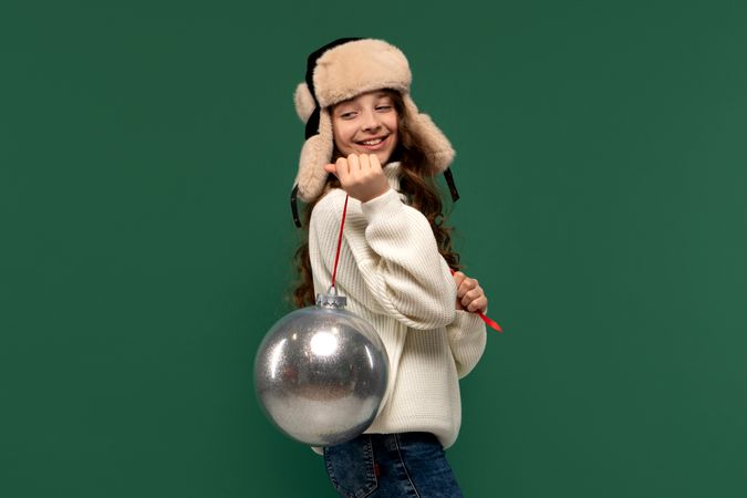 Smiling girl in winter hat holding large silver ornament.